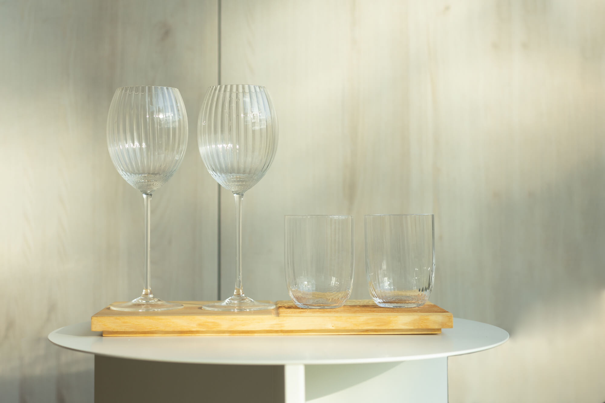 Na stoliku stroi deska do serwowania Fields, na niej od lewej dwa szklane, bezbarwne kieliszki do białego wina i dwie bezbarwne szklanki.