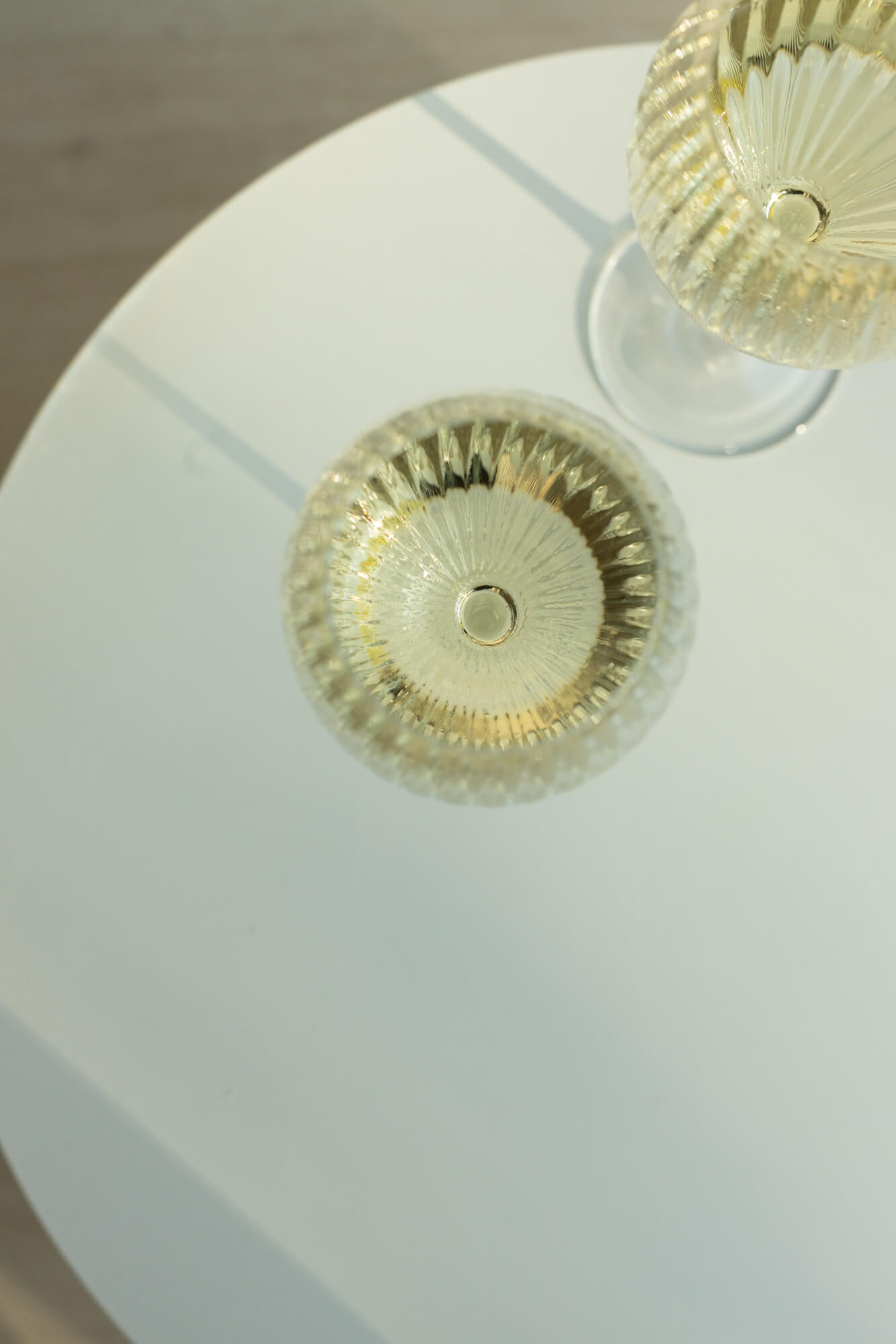 Kadr z góry na dwa szklane, bezbarwne kieliszki do białego wina, stojące na białym stoliku.