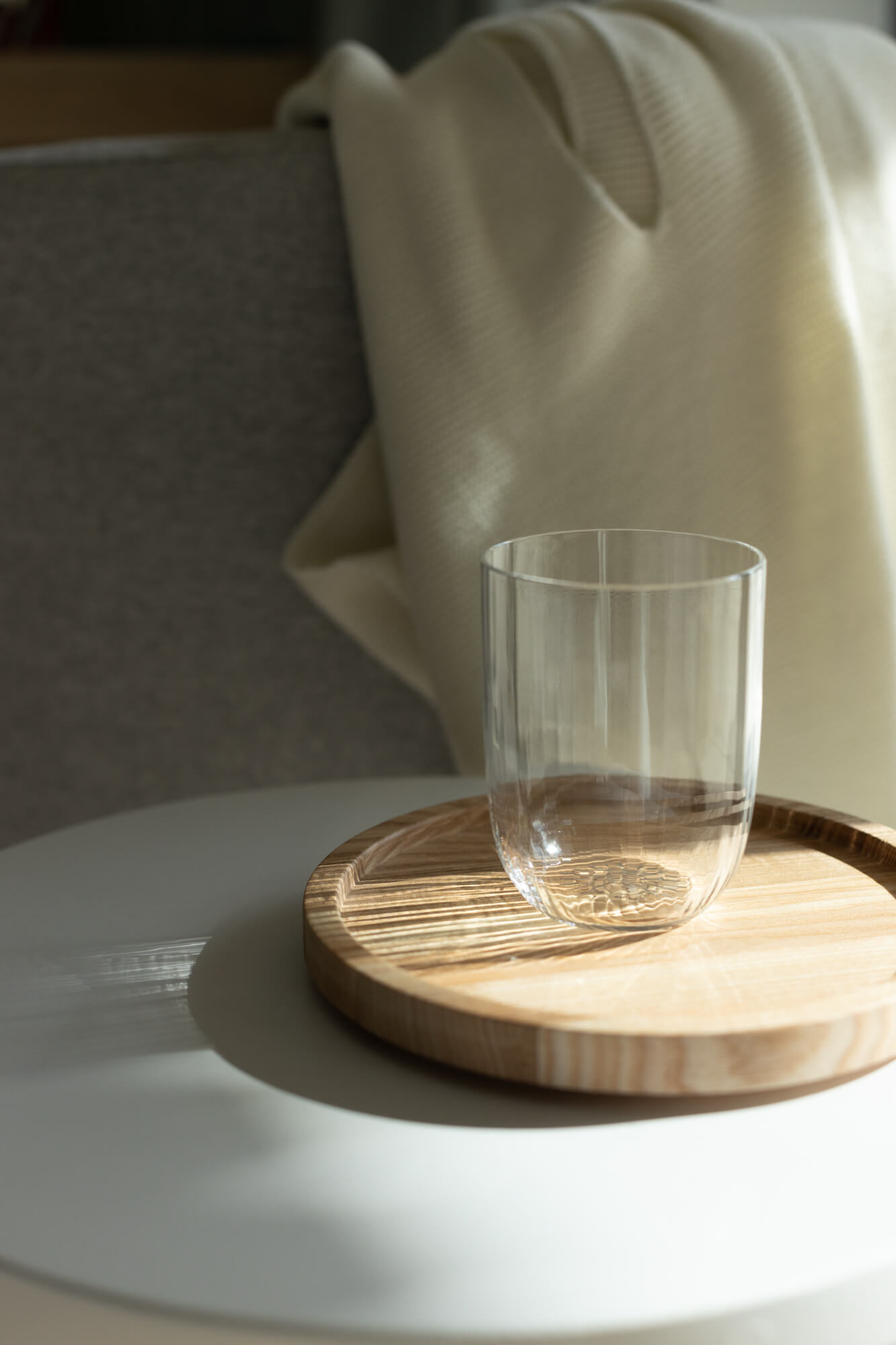 Na okrągłej, drewnianej tacy stoi szklanka.
