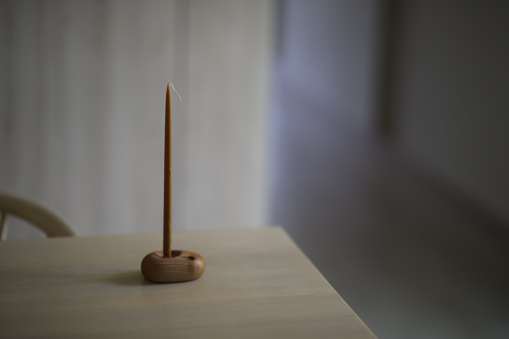 Na stole stoi drewniany świecznik ze świecą z naturalnego wosku pszczelego.