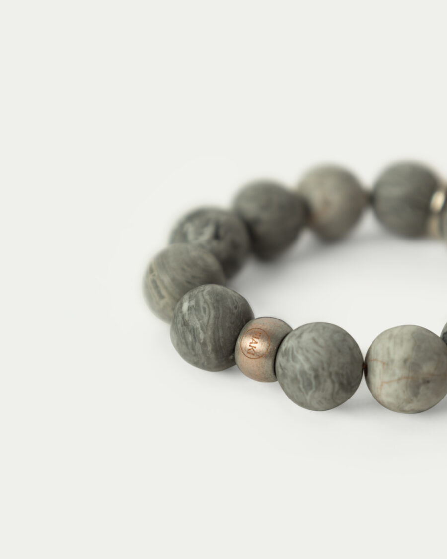 Obrączka na serwetkę. Zbliżenie na okrągłe kamienie naturalne szarego jaspisu i miedzianą przelotkę z logiem MAKI.