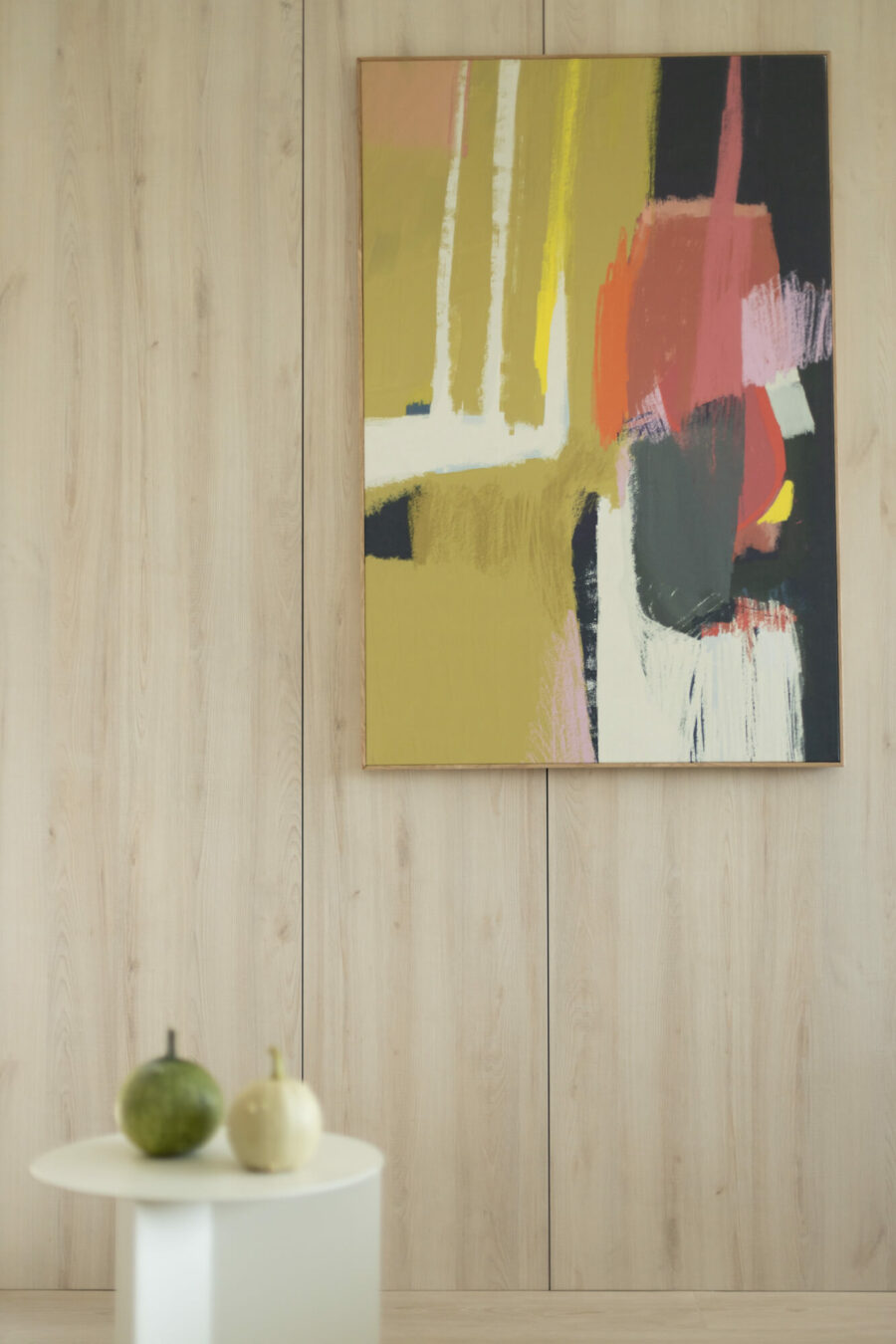 Kolorowy obraz abstrakcyjny wisi na ścianie. Przed nim po lewej stronie stoi biały, okrągły stolik.