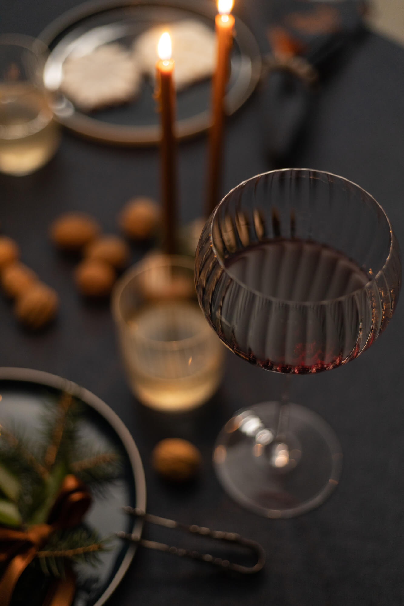 Nakrycie świątecznego stołu. Kieliszek do czerwonego wina i świeczki z wosku pszczelego w świecznikach drewnianych.