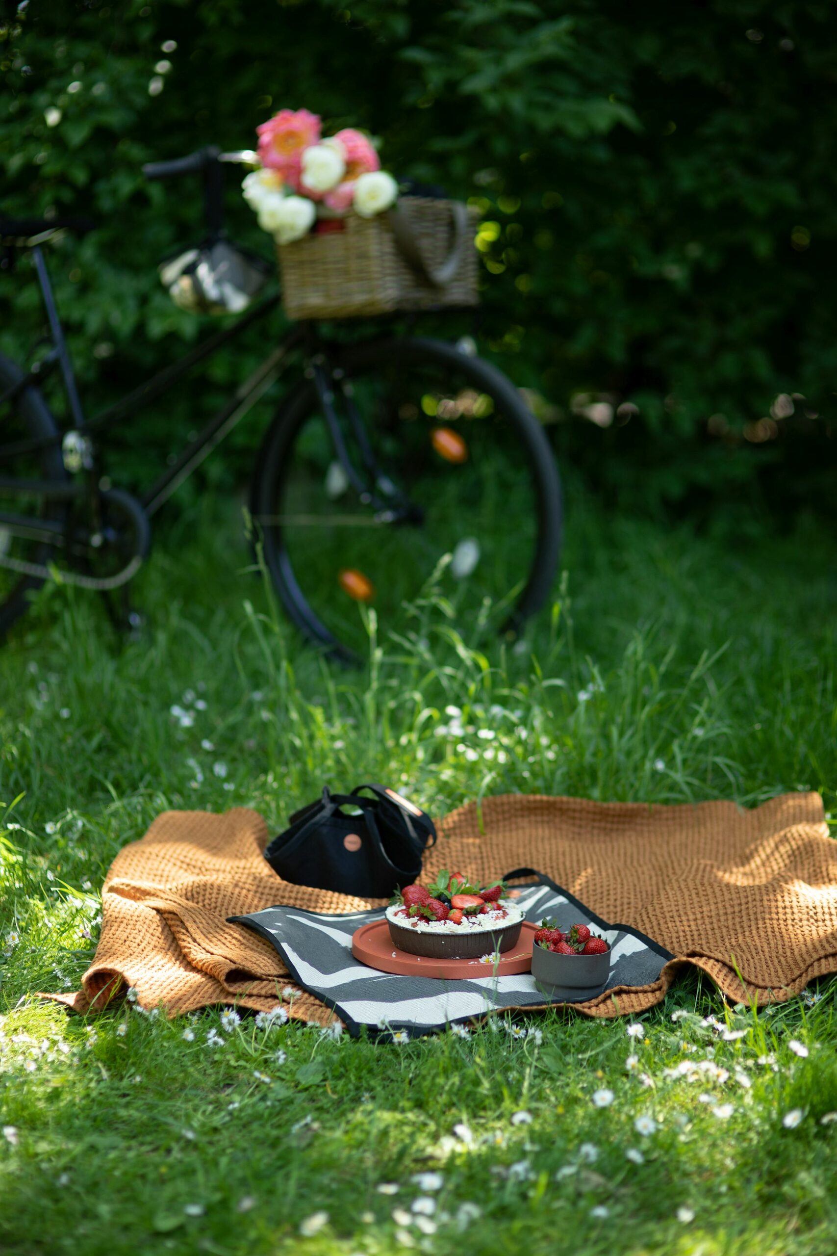 Piknik na trawie. Na trawie leży miedziany pled wafelkowy, na nim rozłożone nosidło piknikowe jako podkładka pod okrągłą, pomarańczową tacę z ciastem truskawkowym.