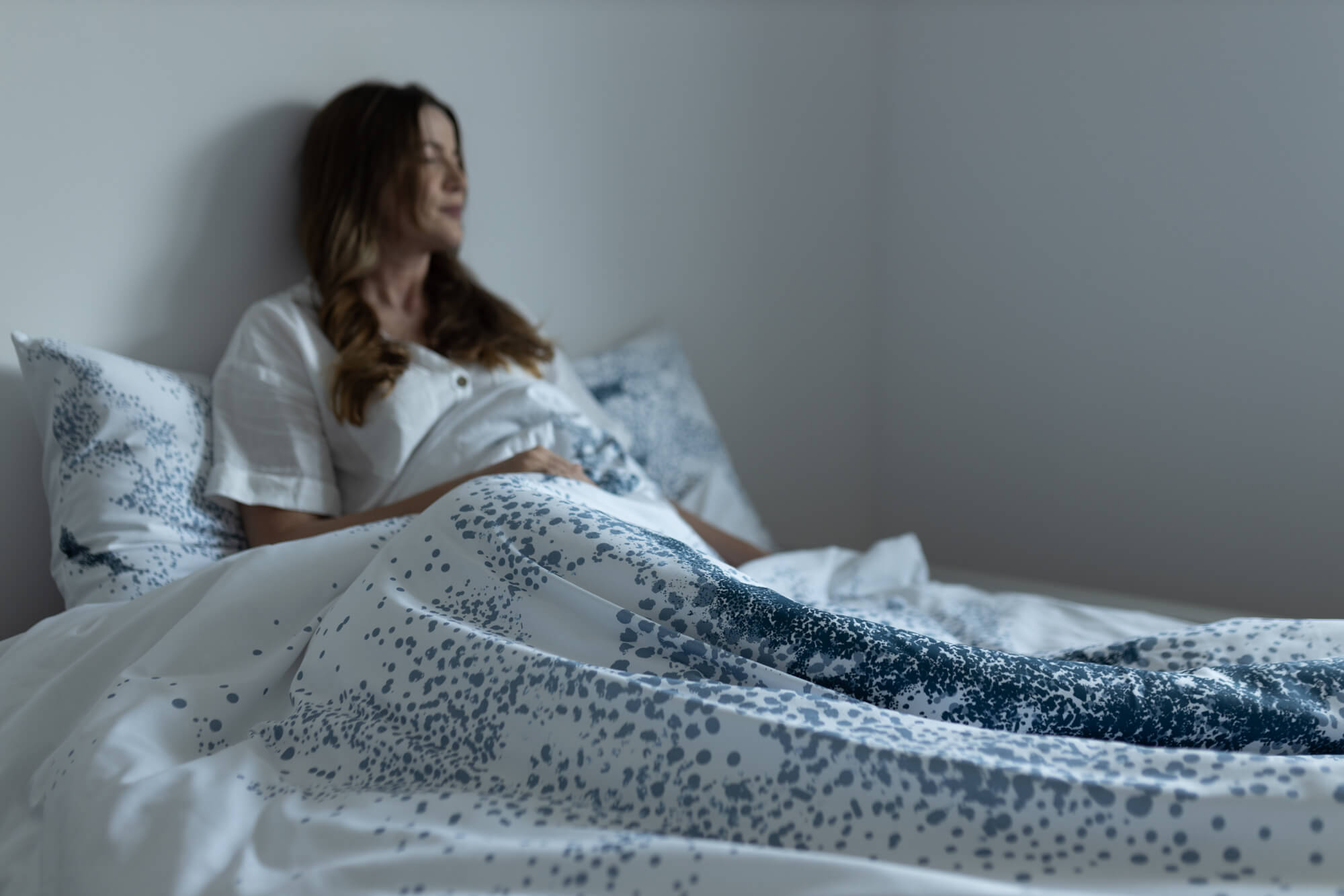 Kobieta siedząca w łóżku zasłanym bawełnianą pościelą z nadrukiem Poppy.