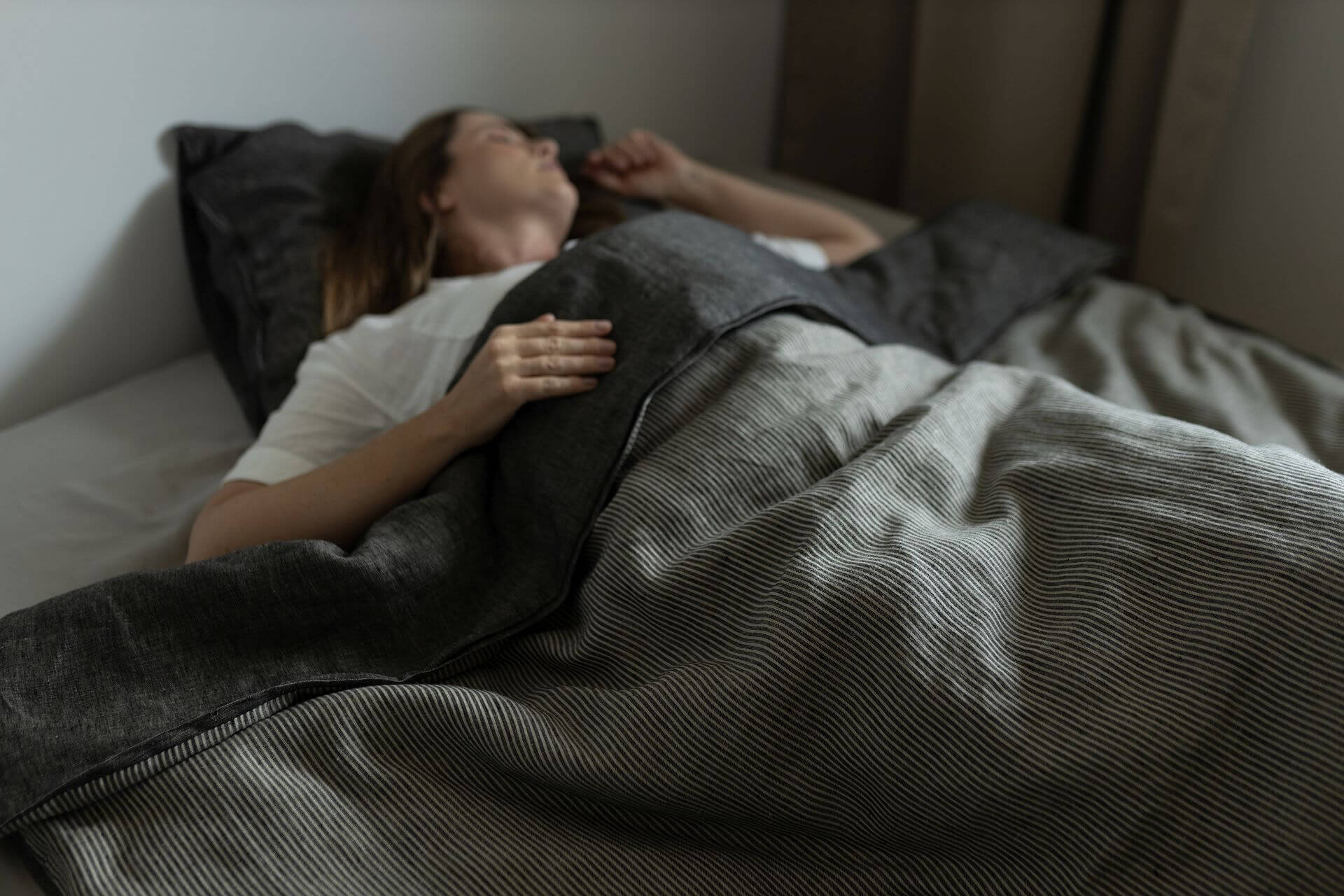 W łóżku śpi kobieta. Przykryta jest lnianą pościelą z well mood.