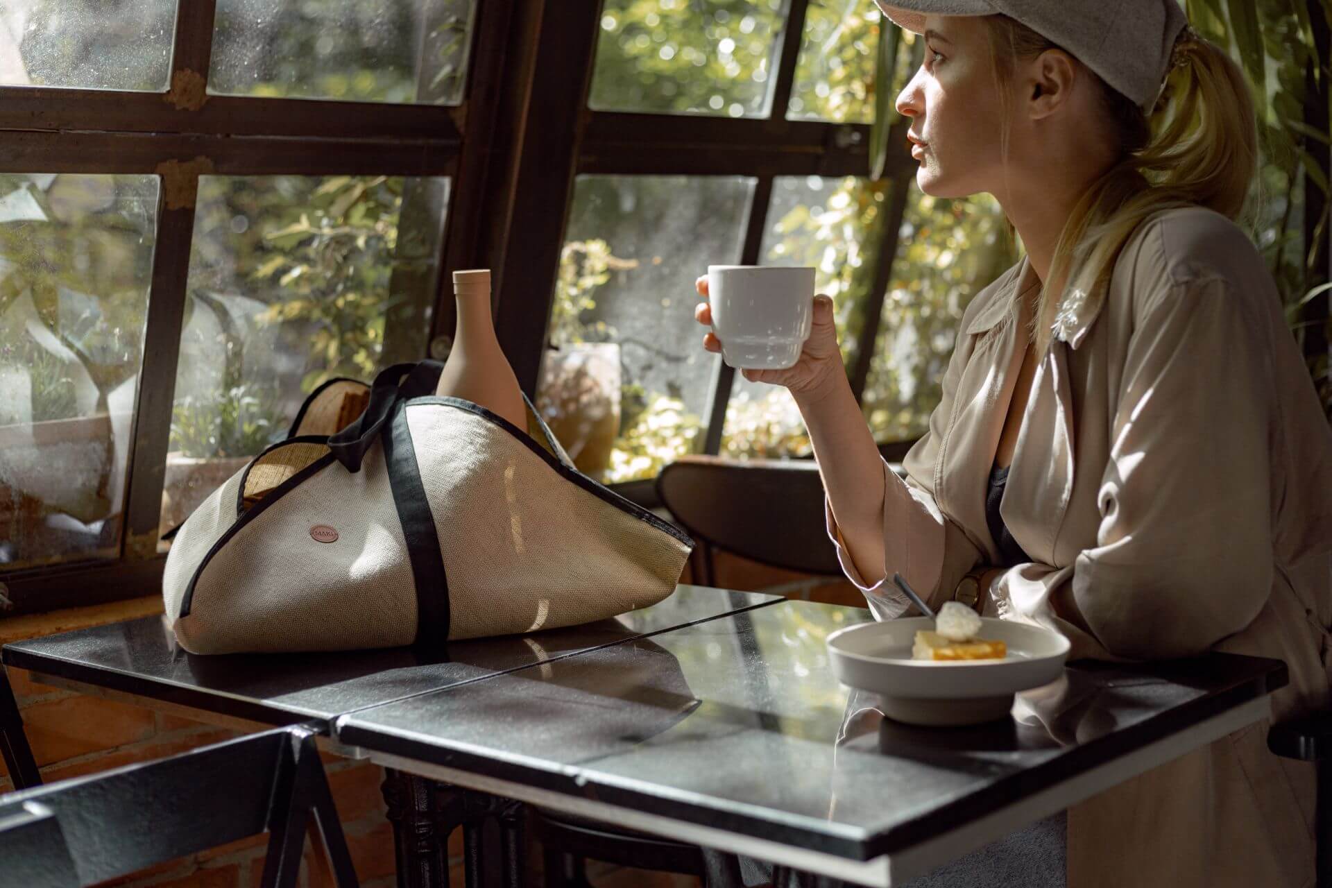 kobieta siedząca przy stole, pijąca kawę z kubka porcelanowego. Na stole leży lniana torba shopperka.