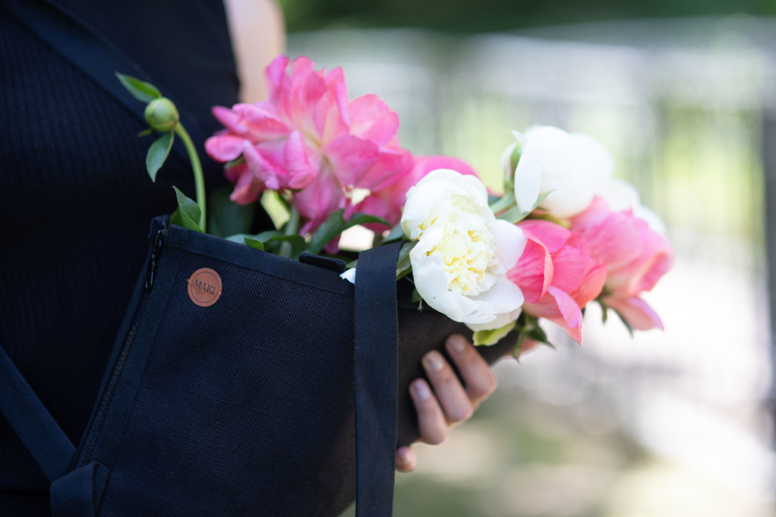 W czarnym lnianym nosidle na kwiaty postać trzyma rozkwitnięte różowe i białe piwonie.